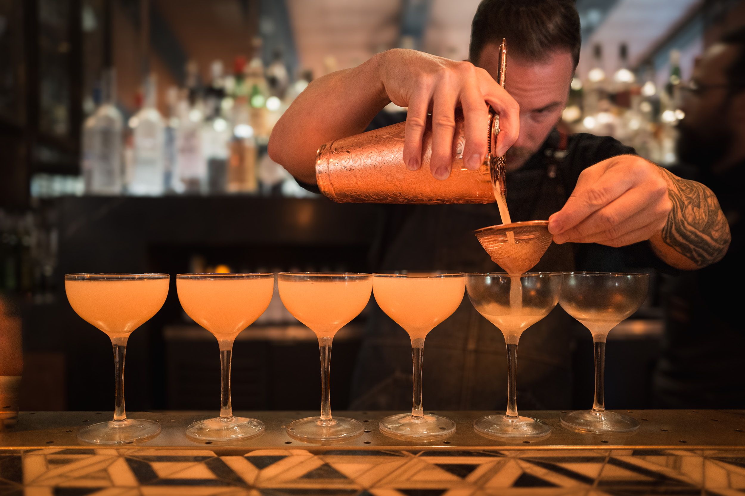 Bartender pouring cocktails into a row of coupes