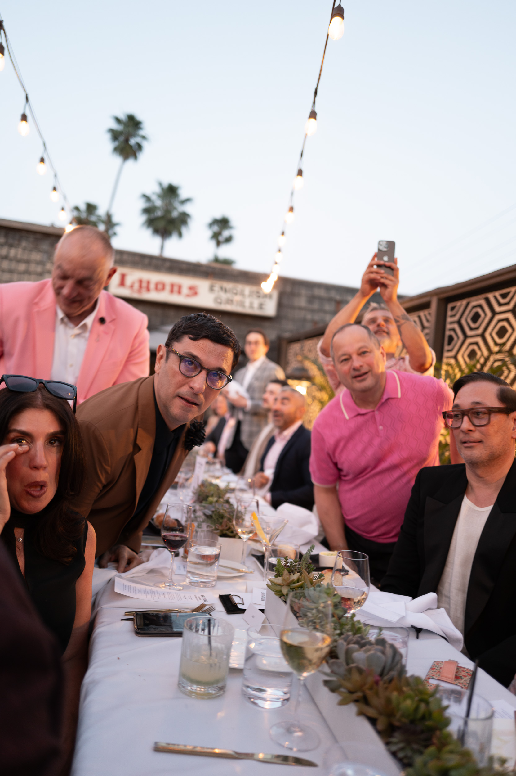 Long outdoor dinner table, string lights, guests mid-conversation