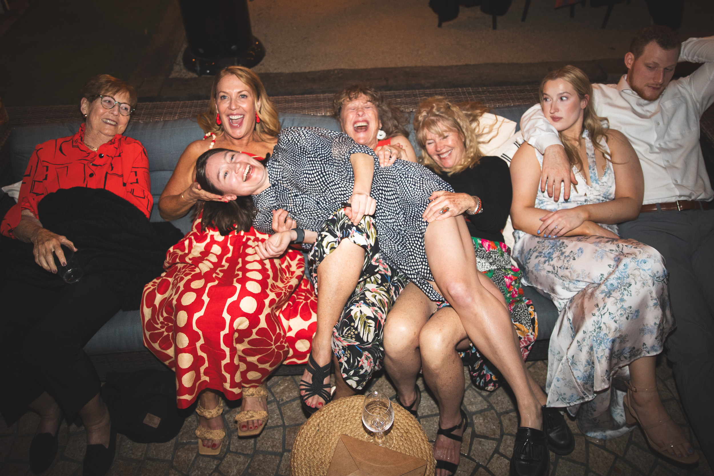 Women piled on a couch, laughing and collapsing, pure chaos