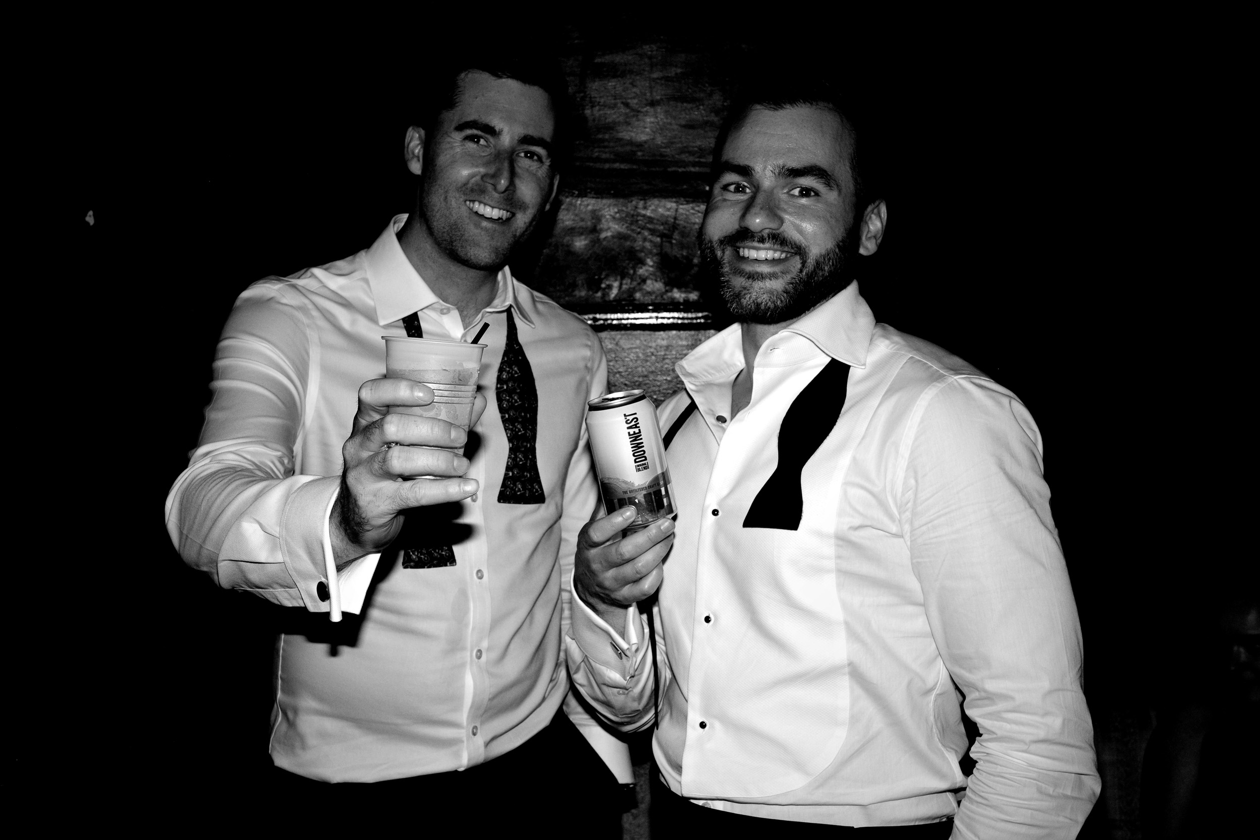 Two groomsmen, black and white, suits and beers